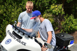 Plymouth Police Academy Cadet shows a visitor a police motorcycle.